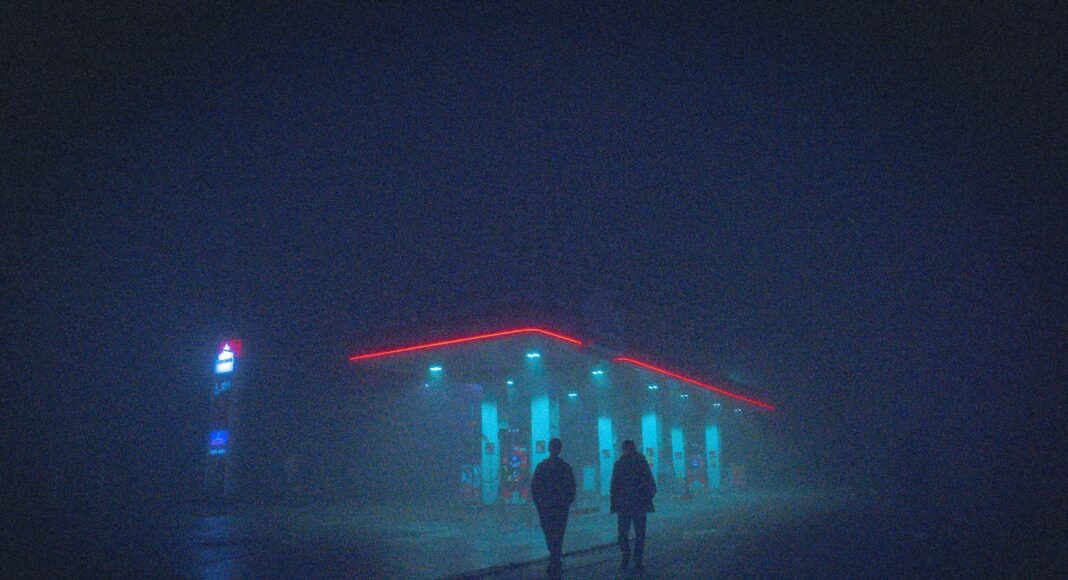a couple of people walking in front of a building with lights