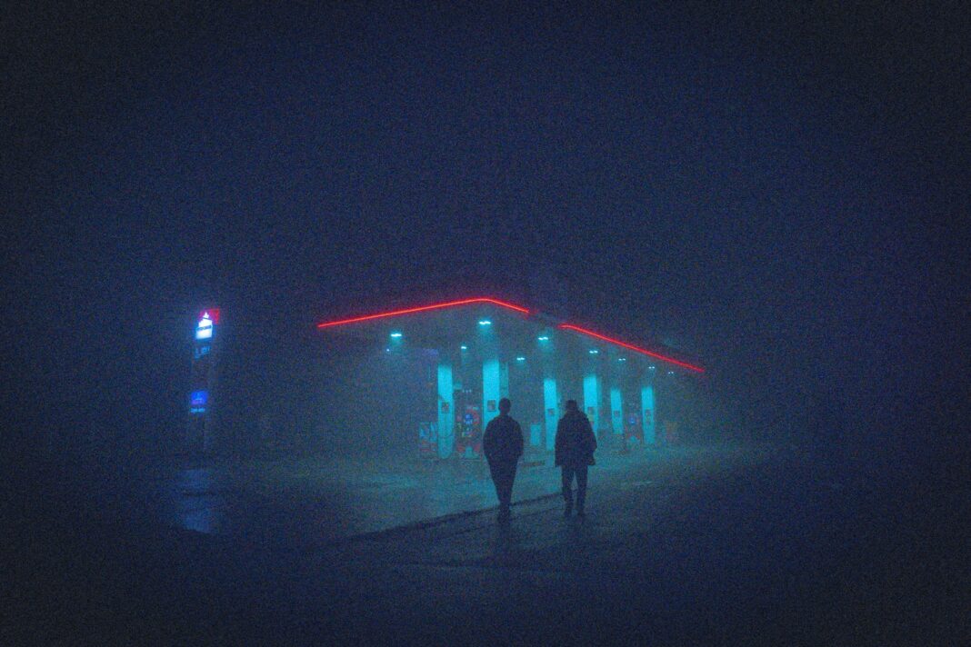 a couple of people walking in front of a building with lights