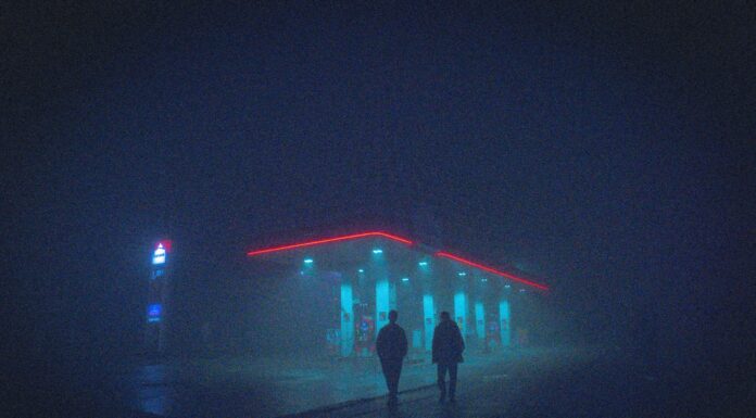 a couple of people walking in front of a building with lights