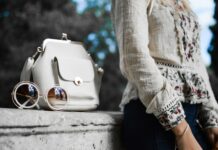 woman wearing beige and red floral top leaning on gray concrete slab with white leather bag ontop
