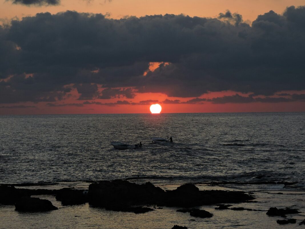 the sun is setting over the ocean with surfers in the water