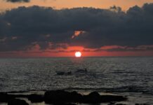 the sun is setting over the ocean with surfers in the water