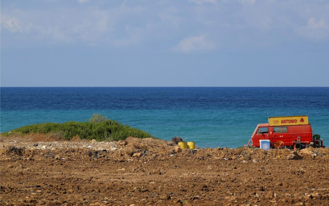 a red van parked on top of a dirt field next to the ocean