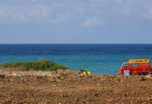 a red van parked on top of a dirt field next to the ocean