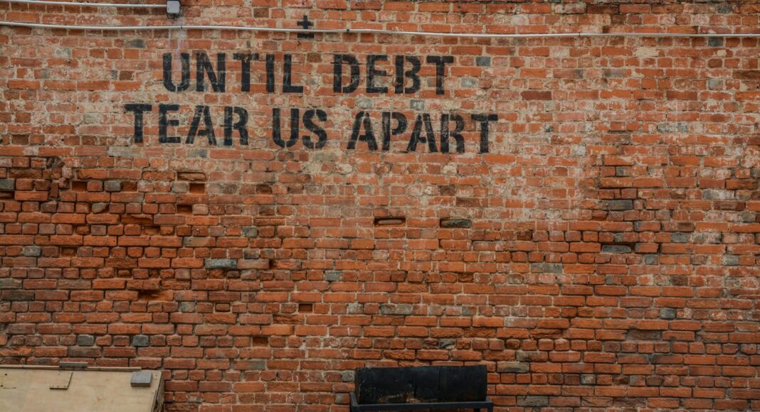 Until debt tear us apart printed red brick wall at daytime